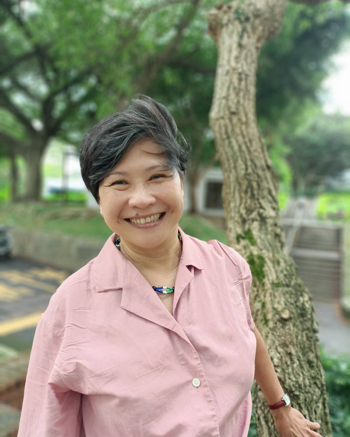 Anisah in pink, standing next to a tree trunk with blurred background